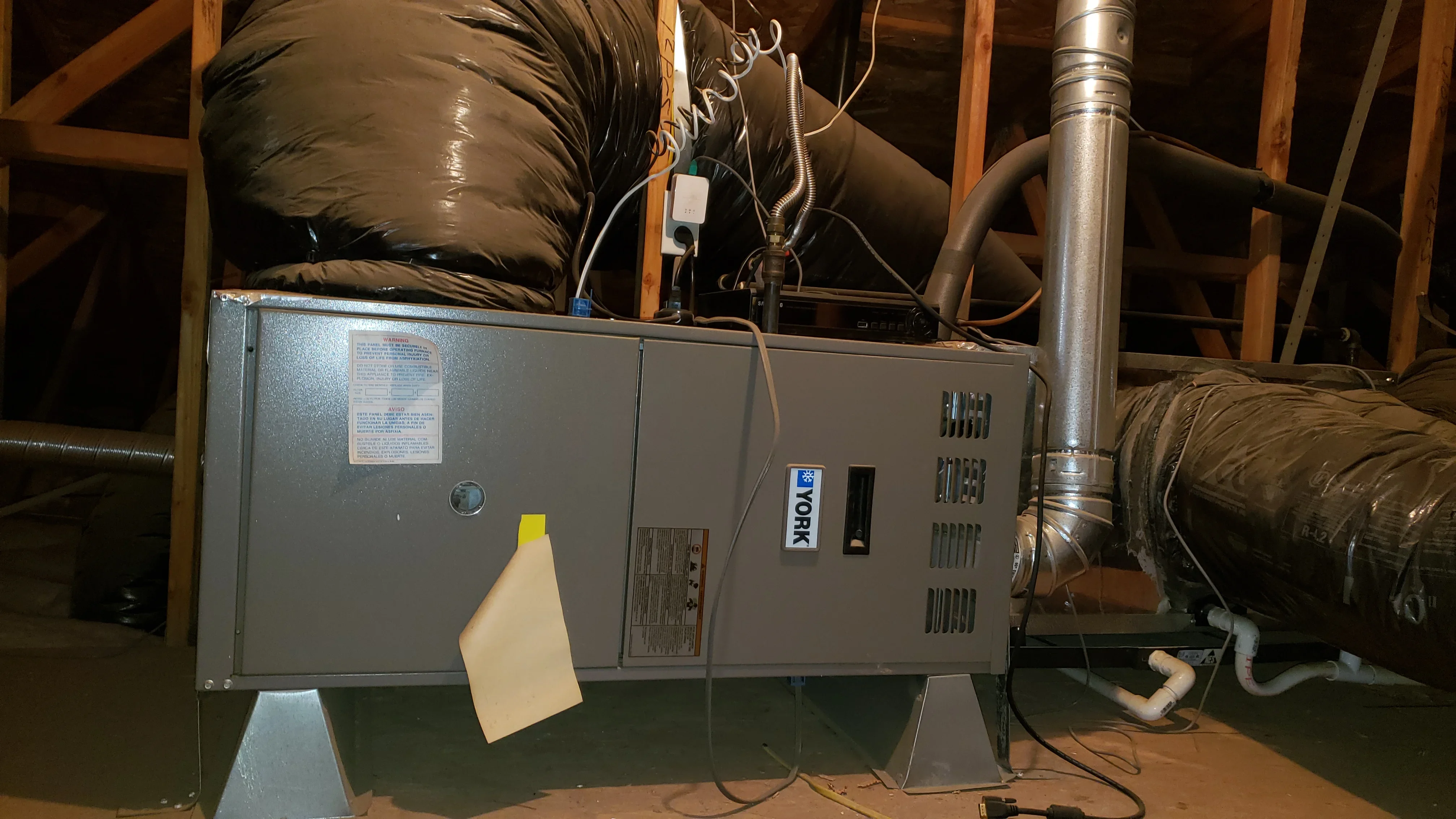 Newly installed HVAC unit in attic with insulated ducts and metal piping
