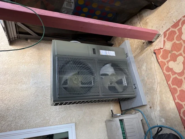 Through-wall AC unit installed under pink metal bracket with dual fans and mesh grilles