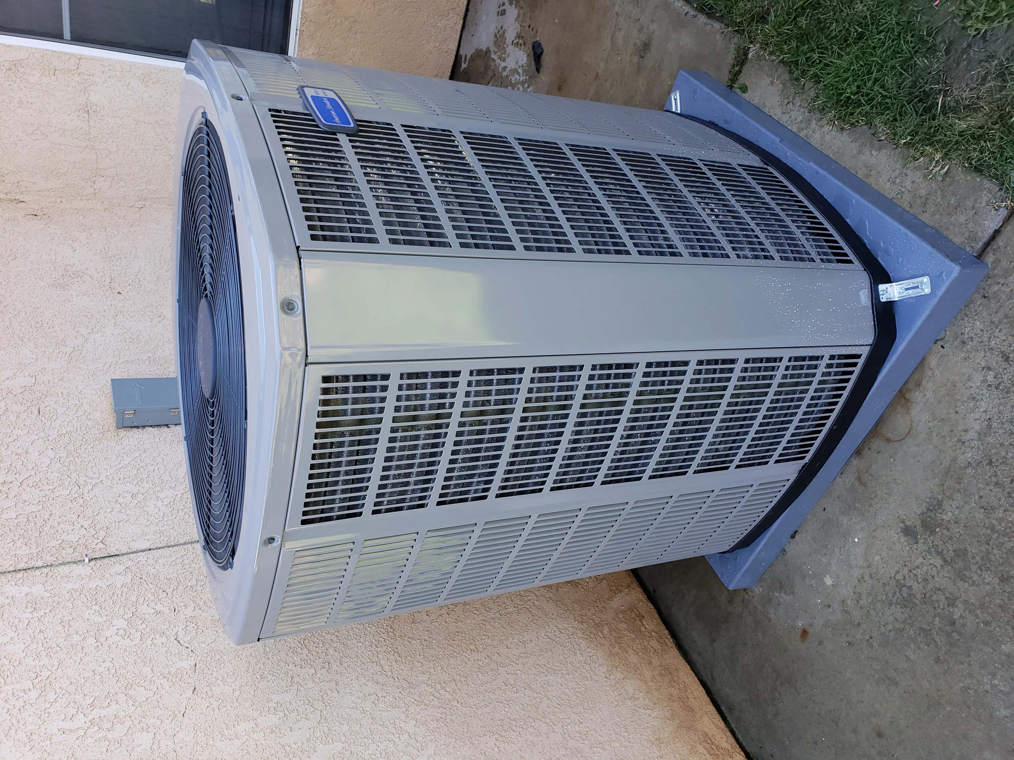 Gray air conditioning condenser unit with circular fan motor installed on concrete pad