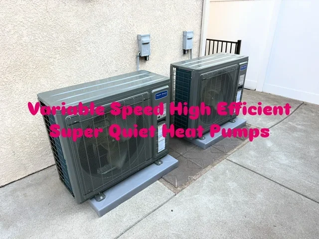 Two gray heat pump units installed side-by-side on concrete foundation pads