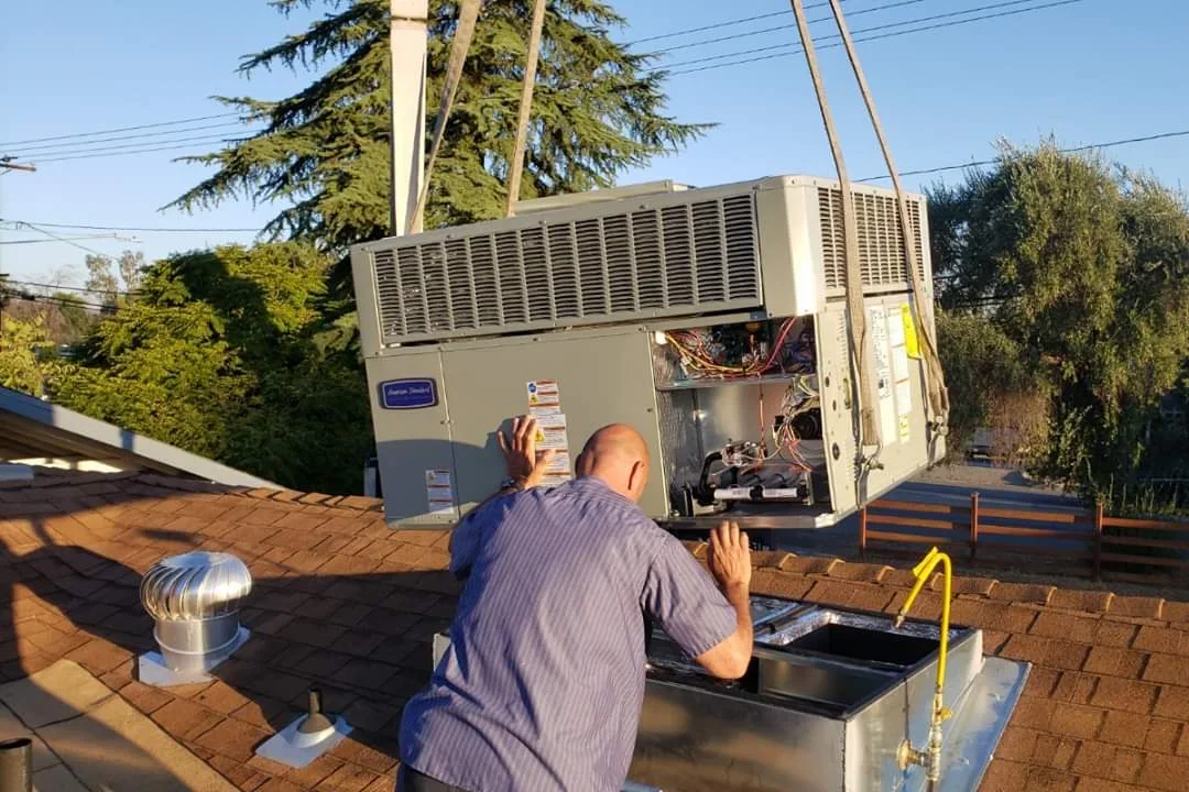 HVAC technician installing rooftop package unit with condenser coils visible