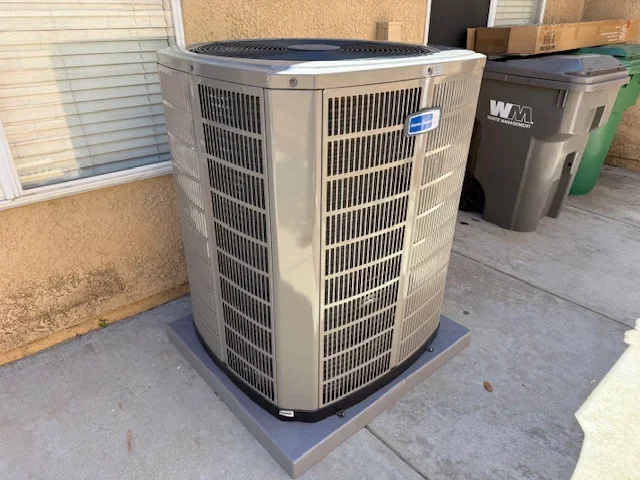 New beige air conditioning condenser unit installed on concrete pad outside residential home